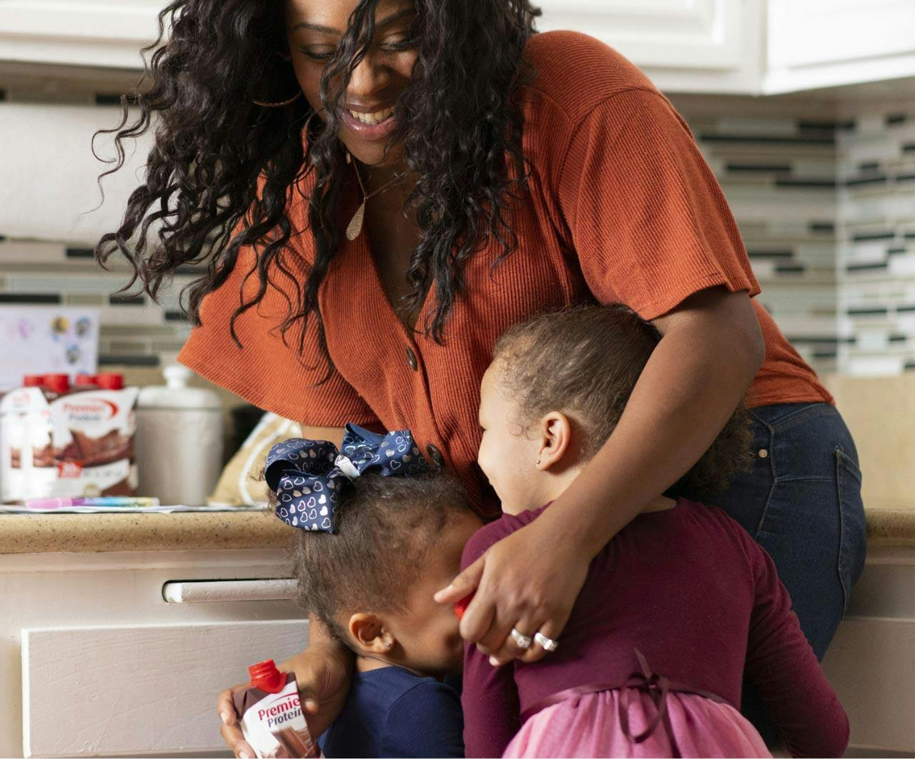 A women hugging her active kids while in her kitchen.