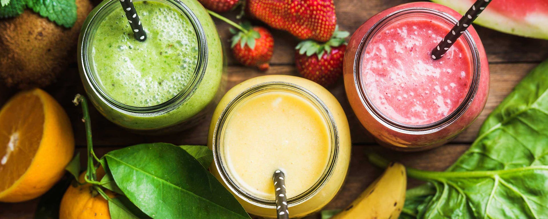 Three multicolored smoothies in jars with straws.