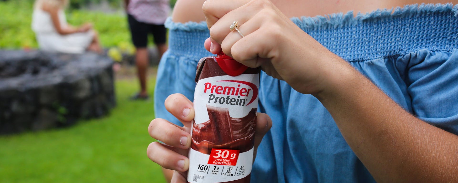 A woman opening a Canadian Chocolate Premier Protein shake at a social gathering.
