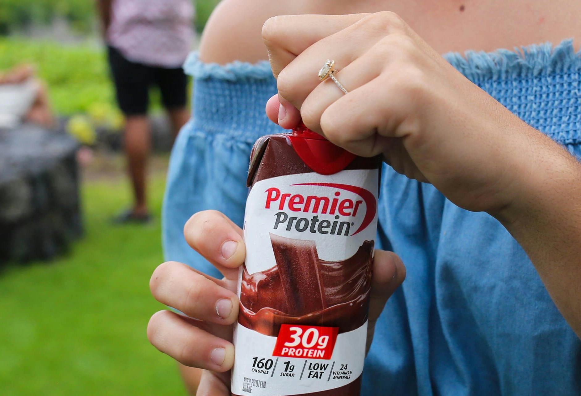 A woman opening a Chocolate Premier Protein shake at a social gathering.