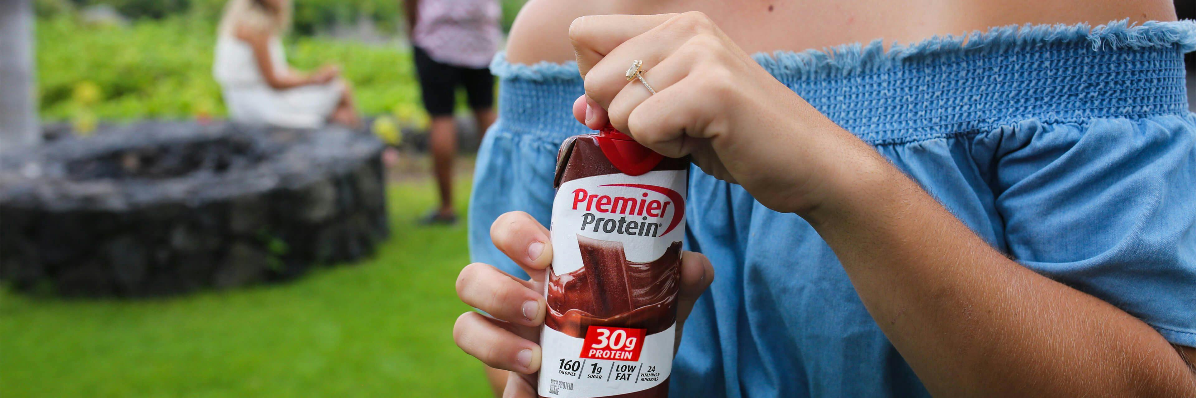 A woman opening a Chocolate Premier Protein shake at a social gathering.