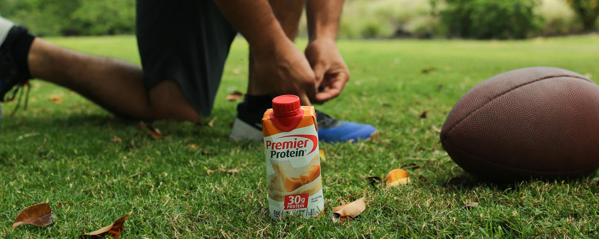 An athlete with a Premier Protein drink and a football.