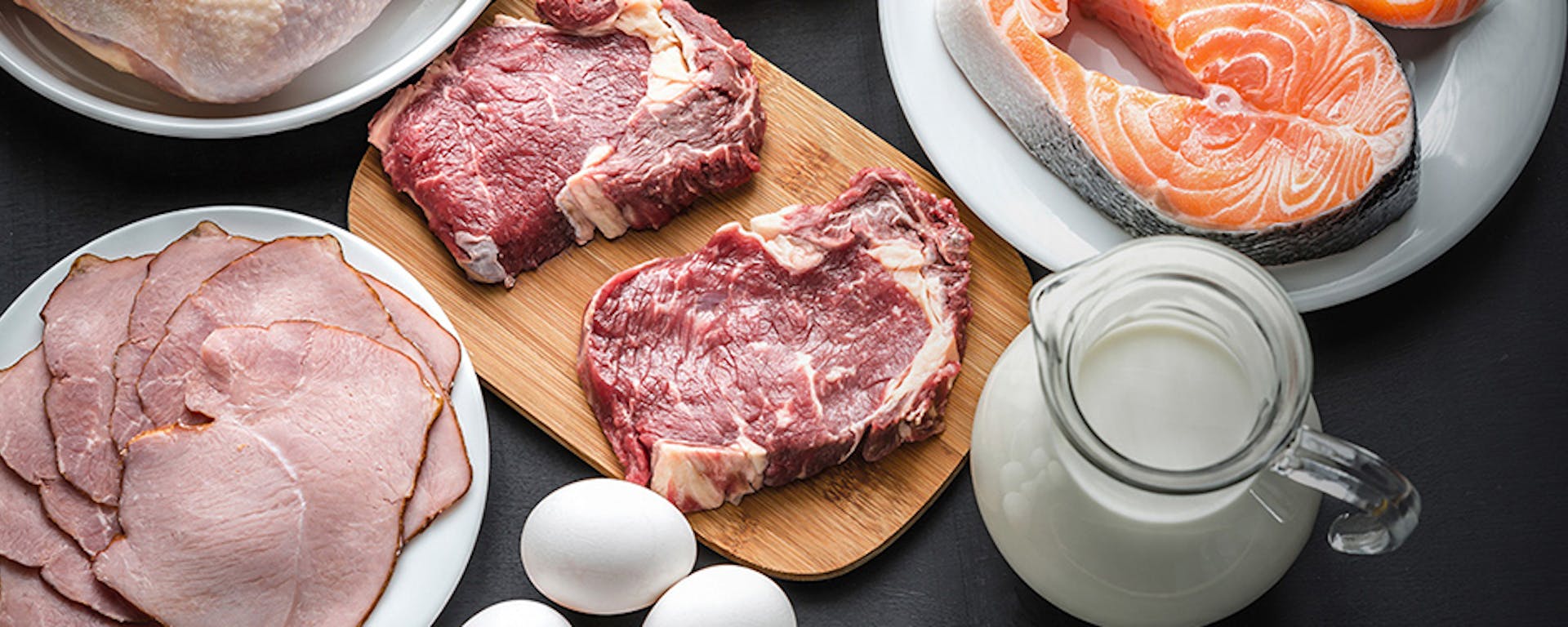 Plates full of meat, fish and a bowl of milk.