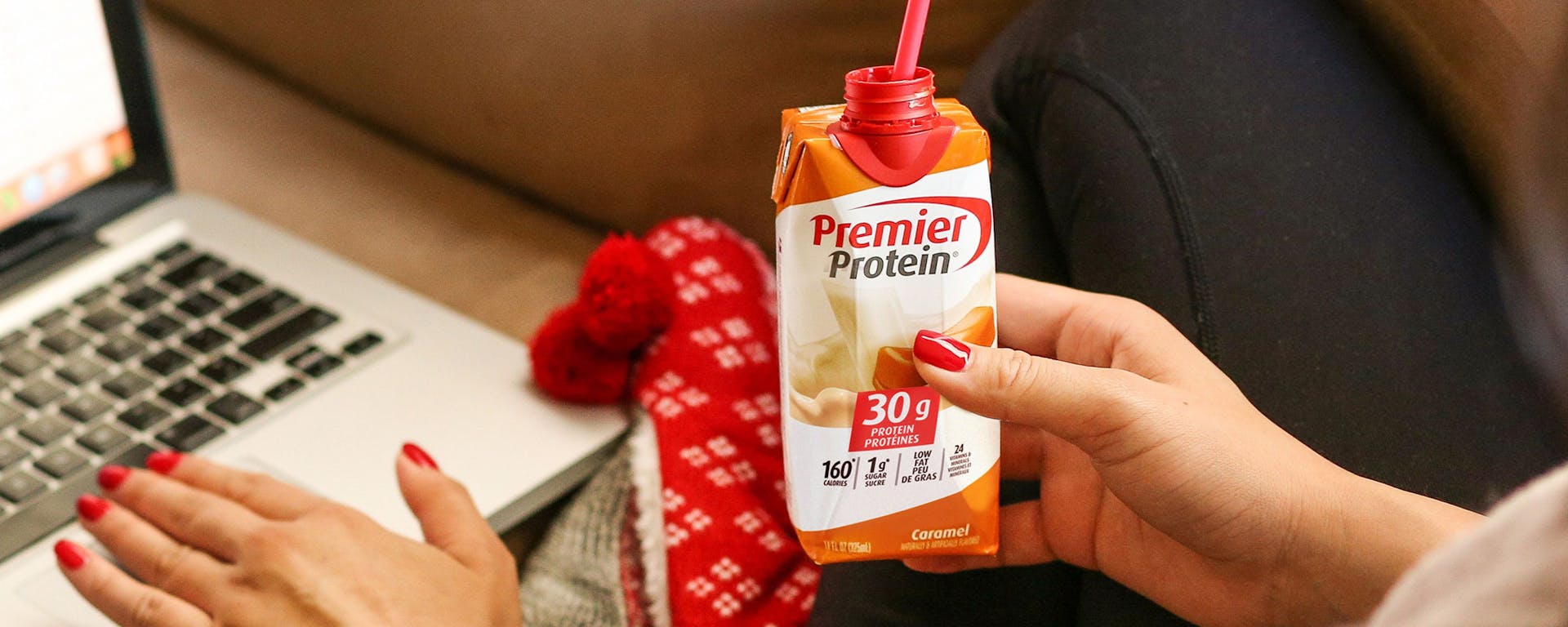 A women at a computer holding a Canadian Premier Protein Caramel Protein Shake