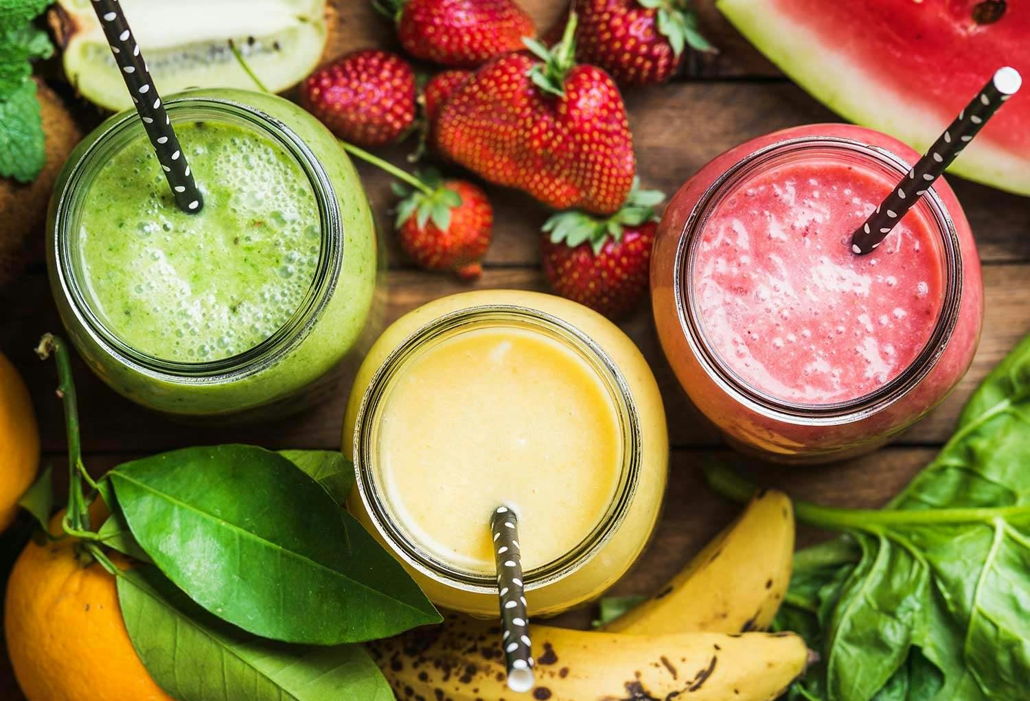 Three multicolored smoothies in jars with straws.