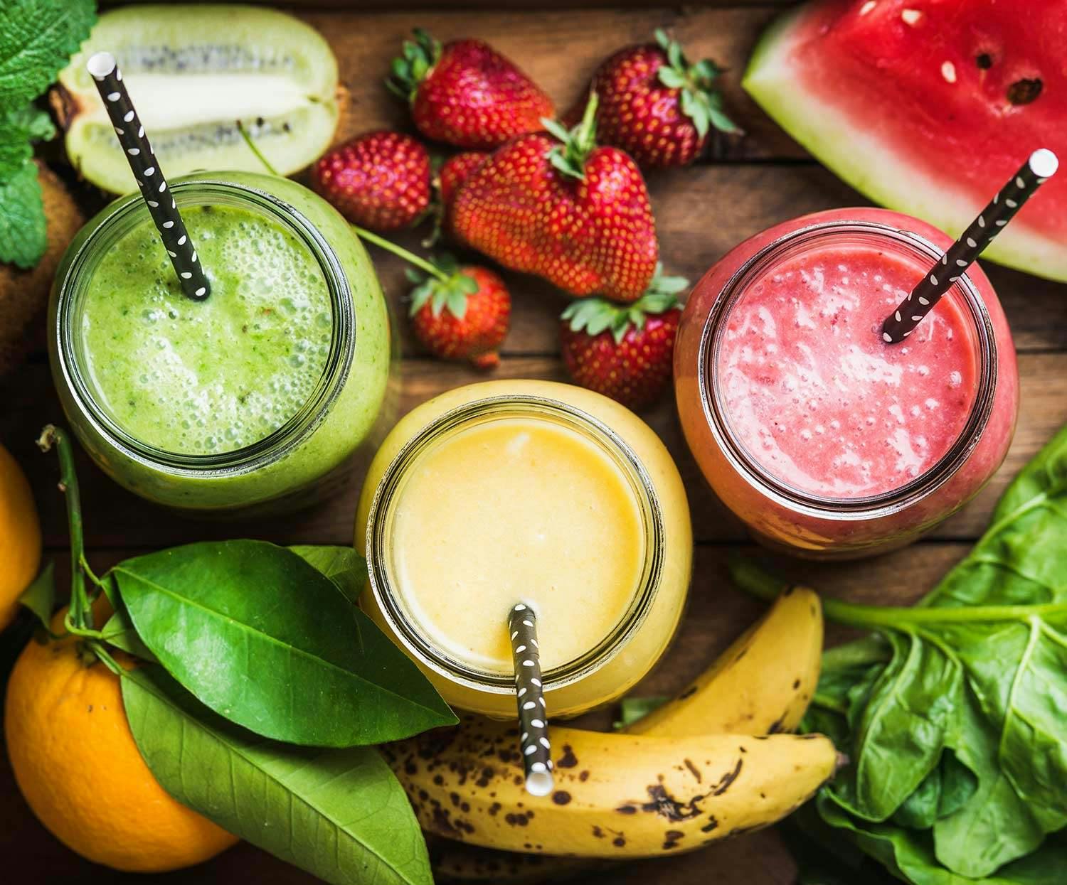 Three multicolored smoothies in jars with straws.