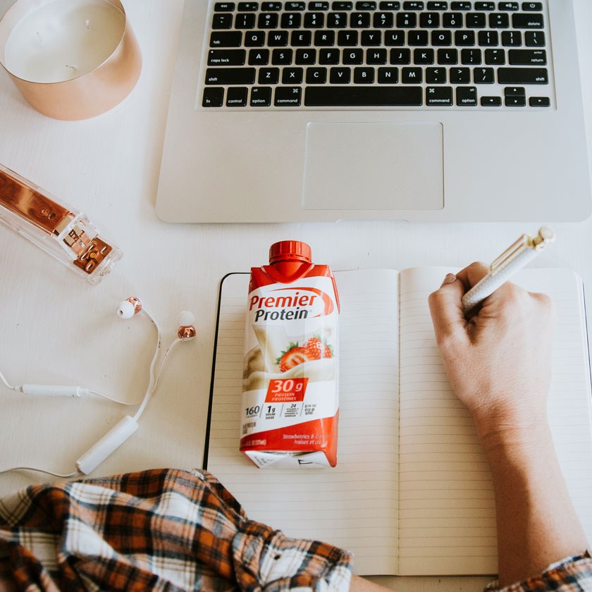 Une boisson protéinée Premier sur table à côté d'un ordinateur portable ouvert.