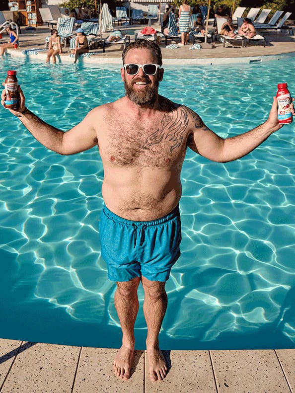 Animated gif of a man falling backwards into a pool holding a premier protein shake in each hand