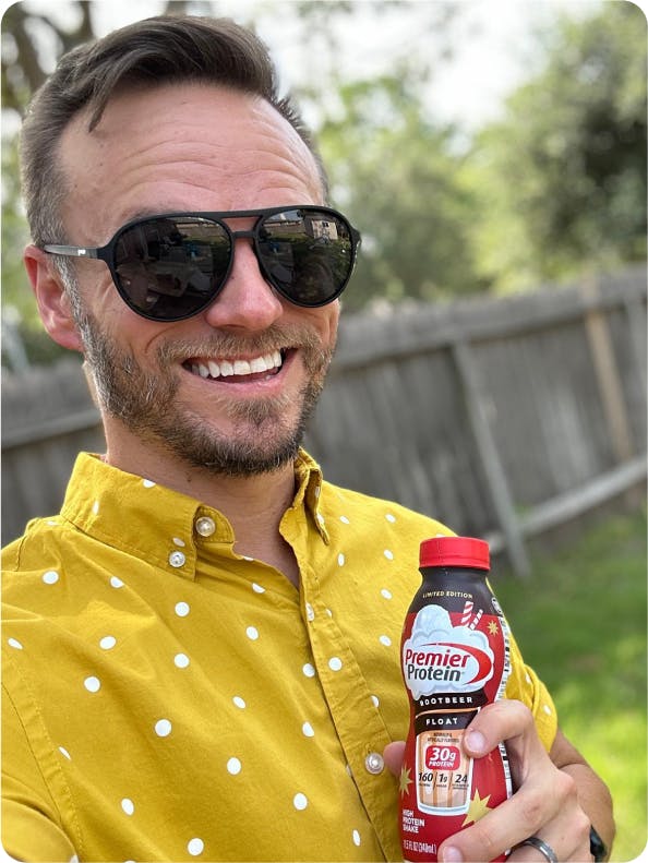 A man with sunglasses smiling while holding a salted caramel popcorn protein shake