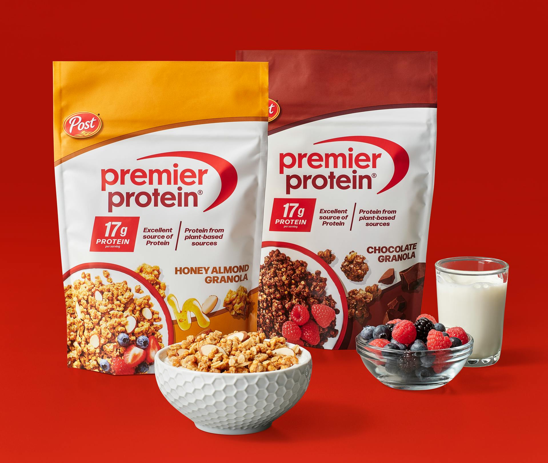 Two bags of Premier Protein granola, along with a bowl of granola, a bowl of berries and a glass of milk.