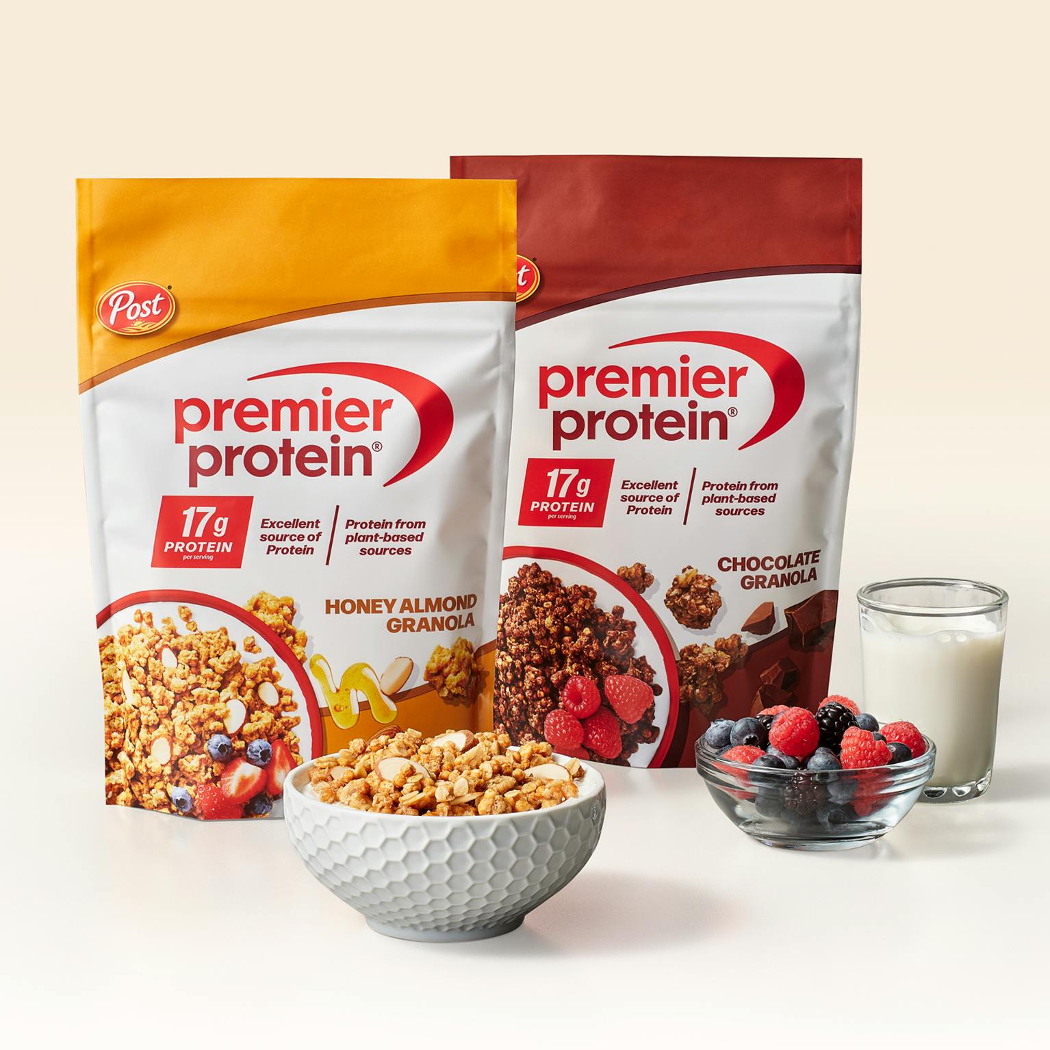 Two bags of Premier Protein Granola in front of bowls of granola and a glass of milk.