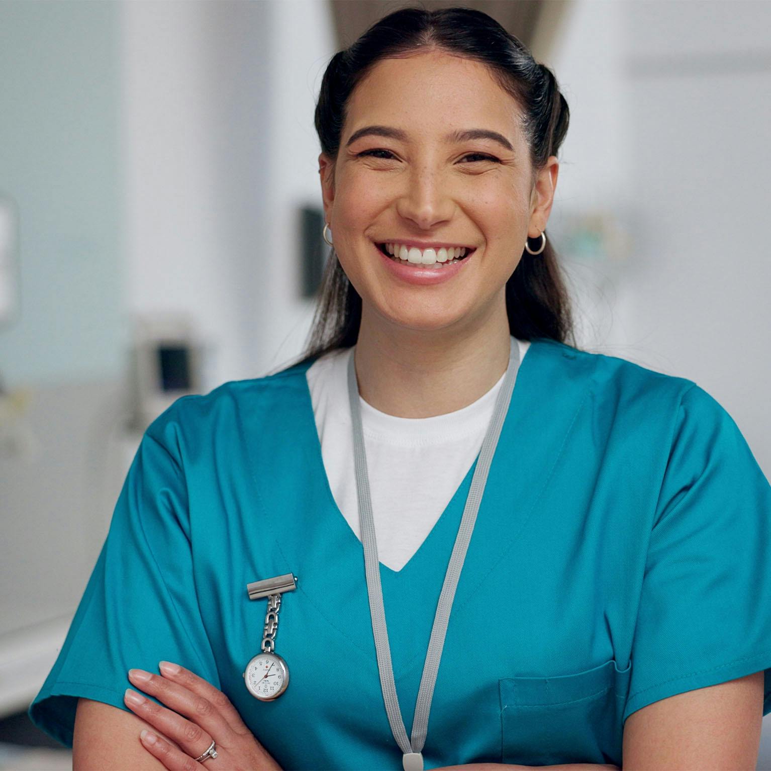 A nurse in teal scrubs smiles for the camera.